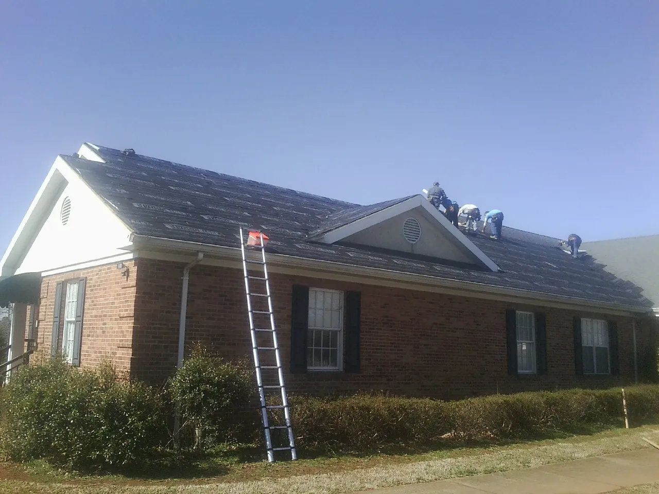 Crew tearing shingles off a brick ranch roof with a ladder set — Metal Roof Repair work by our crew in Barrett