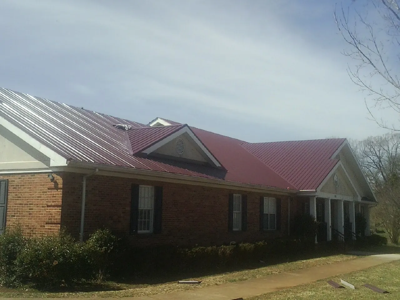 Red metal roof with gabled entries on a long brick building, from a Hail Damage Roof Repair job in Barrett