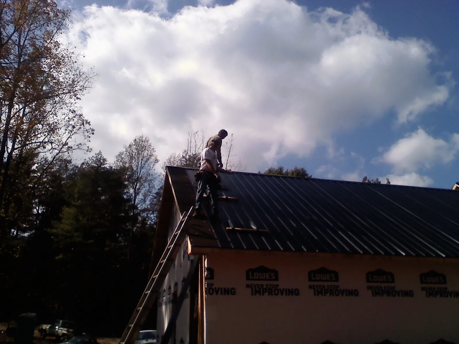Roofer fastening dark metal panels high against a cloudy sky, from a Roof Inspection job in Barrett