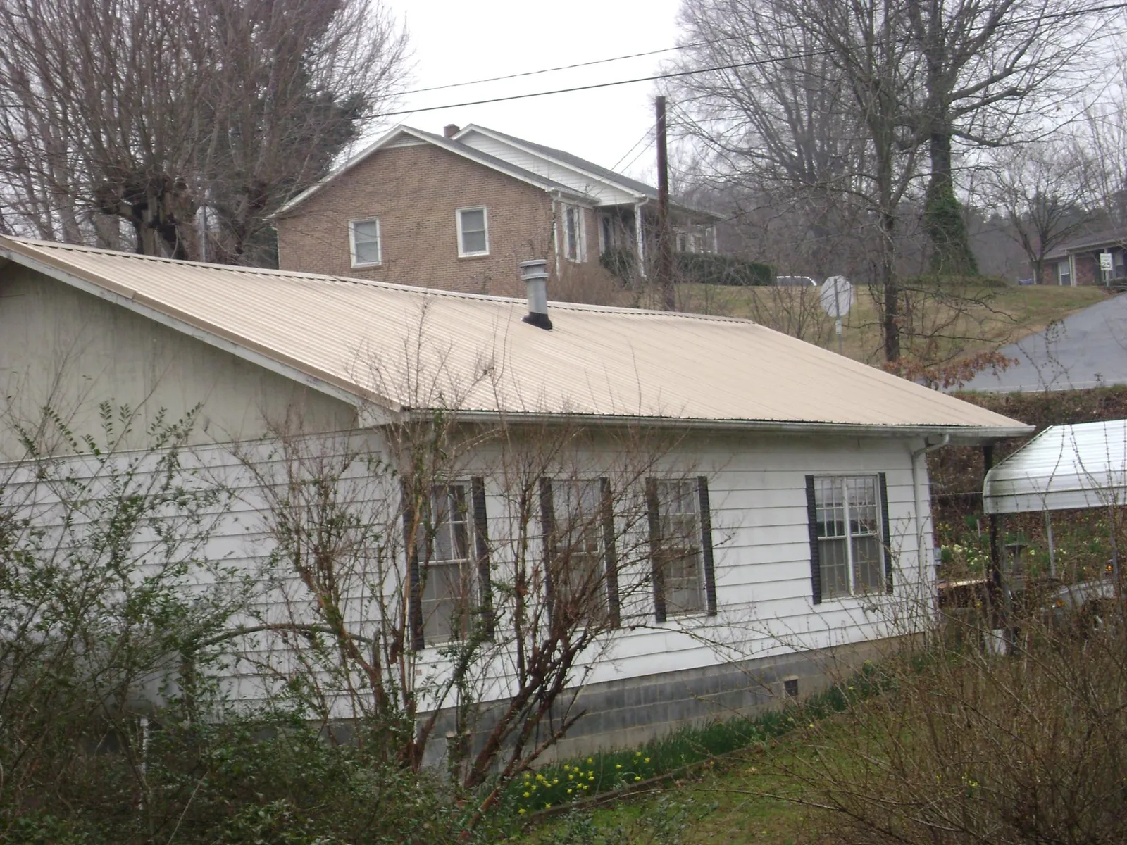 Tan metal roof on a white sided house set into a hillside — Commercial Roofing by Roofing Brothers in Barrett
