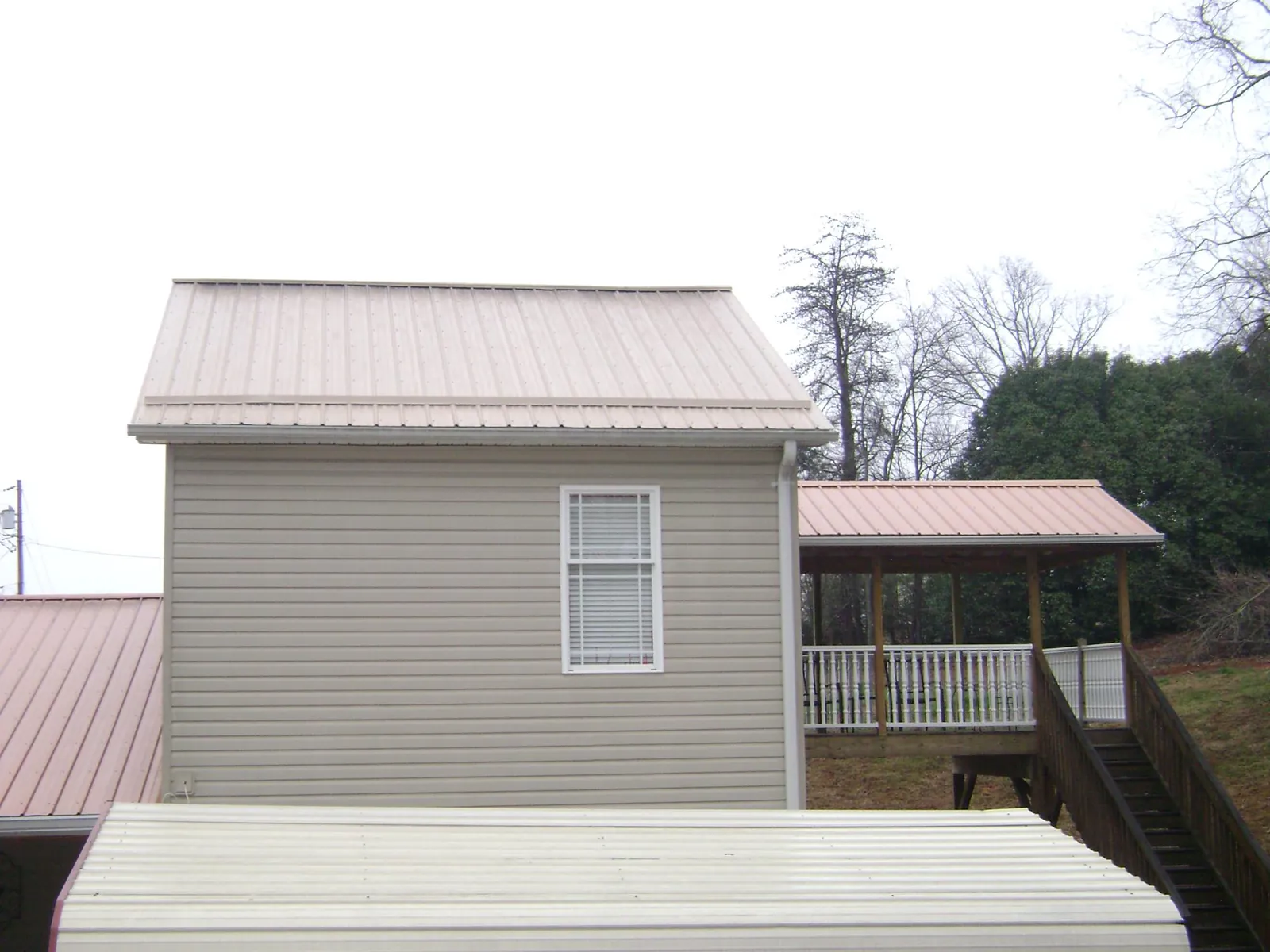 Tan metal roofs on a two story addition and attached porch, from a Roof Replacement job in Barrett